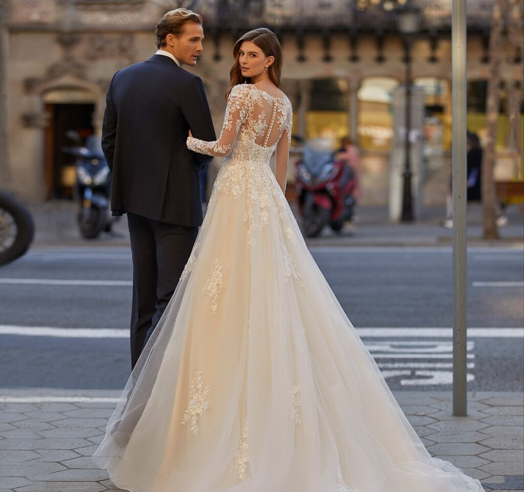 Novia posa con su novio luciendo un traje cargado de transparencias.