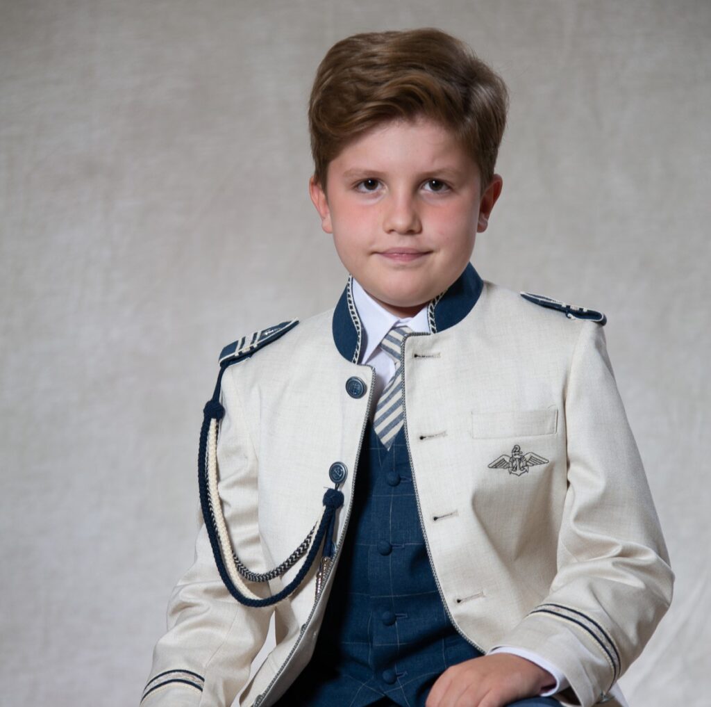 Niño luce un vestido de comunión con una corbata en tonos azules.
